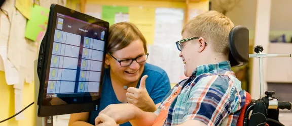 Sonderpädagogische Lehrkraft lernt mit behindertem Kind im Rollstuhl vor einem Monitor