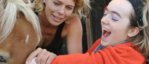 Eine Frau und ein behindertes Kind streicheln ein Pferd am Therapiehof Leila