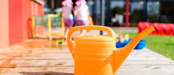 Orangene Gießkanne im Garten der Kindertagesstätte