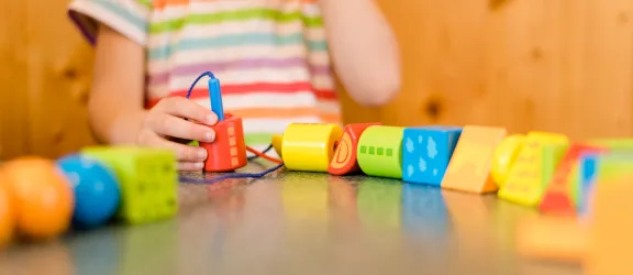 Kind in der Krippe fädelt bunte Holzklötze auf