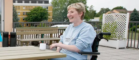 Drei behinderte Menschen sitzen auf einer Terrasse des Wohnheims