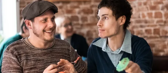 Junger Mann mit Behinderung isst mit seinem Betreuer ein Eis