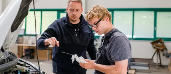 Azubi und Ausbilder stehen vor einer offenen Motorhaube