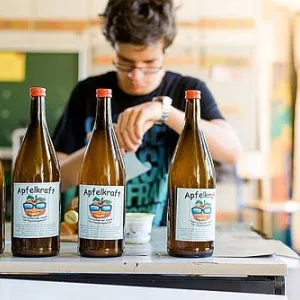 Vier Apfelsaftflaschen stehen vor einem Jugendlichen auf dem Tisch