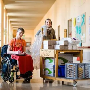 Ein junger Mensch im Rollstuhl mit einer Mitarbeiterin im Flur