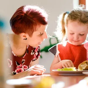 Erzieherin hilft Krippenkind beim Essen