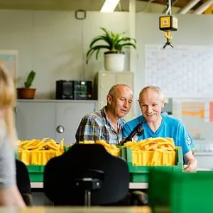 Drei Menschen stehen in der Werkstatt an Tischen
