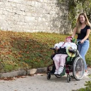 Mitarbeiterin schiebt eine Beschäftigte im Rollstuhl im Garten