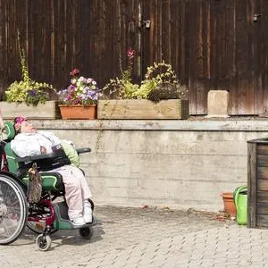 Mitarbeiterin schiebt eine Beschäftigte im Rollstuhl über den Hof