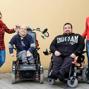 Vier Menschen - zwei stehen, zwei sitzen im Rollstuhl