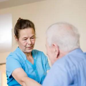 Pflegefachkraft mit Bewohner im Zimmer bei Grundpflege