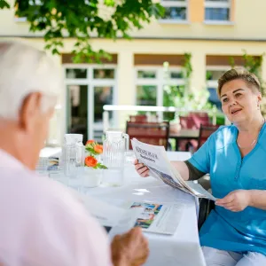 Pflegefachkraft mit Bewohnerin beim Zeitunglesen im Garten