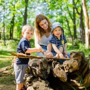 Pädagogin mit zwei Kleinkindern im Wald vor einem Baumstumpf
