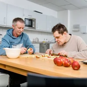 Zwei Menschen mit Behinderung sitzen an einem Tisch und schälen Äpfel