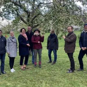 Neun Menschen stehen auf der Streuobstwiese vor einem Baum