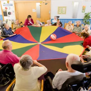 Viele Menschen sitzen im Kreis und haben ein buntes Tuch in der Hand