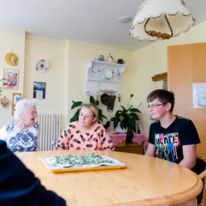 Zwei alte Frauen und ein Schüler sitzen an einem Tisch