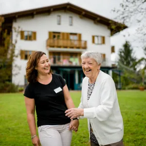 Seniorin mit Pflegefachkraft vor Parkwohnanlage