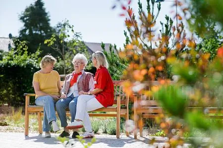Seniorin mit Besucherin und Mitarbeiterin auf einer Bank vor Seniorenzentrum Gottfried Seiler Feucht