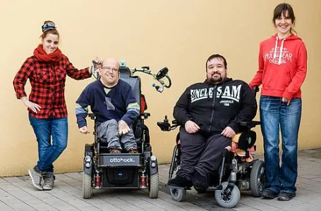 Vier Menschen - zwei stehen, zwei sitzen im Rollstuhl