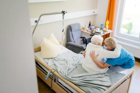 Pflegefachkraft hilft Seniorin beim Aufstehen aus dem Pflegebett