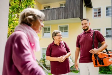 2 ambulante Pflegefachkräfte mit Seniorin vor dem Haus