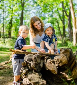 Pädagogin mit zwei Kleinkindern im Wald vor einem Baumstumpf