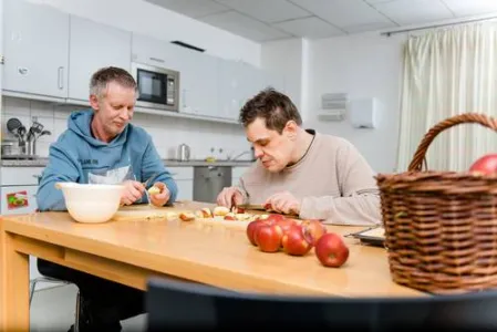 Zwei Menschen mit Behinderung sitzen an einem Tisch und schälen Äpfel
