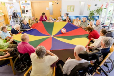 Viele Menschen sitzen im Kreis und haben ein buntes Tuch in der Hand