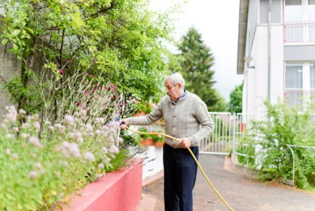 Alter Mann gießt mit einem Schlauch Blumen