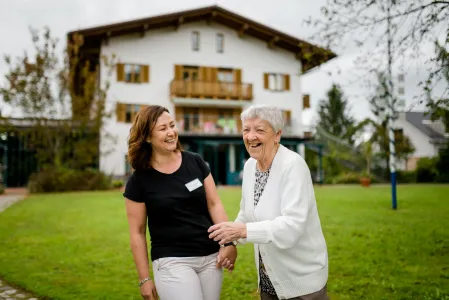 Seniorin mit Pflegefachkraft vor Parkwohnanlage