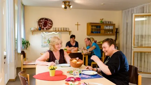 Vier Menschen sitzen in einem Raum an zwei Tischen und sprechen miteinander