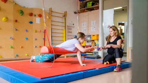 Ein Mädchen liegt über eine Schaukel und spielt mit einer Mitarbeiterin