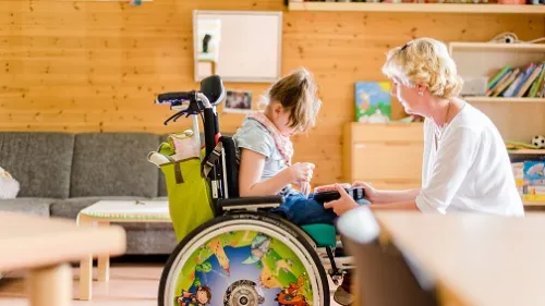 Kind im Rollstuhl spricht mit einer Mitarbeiterin
