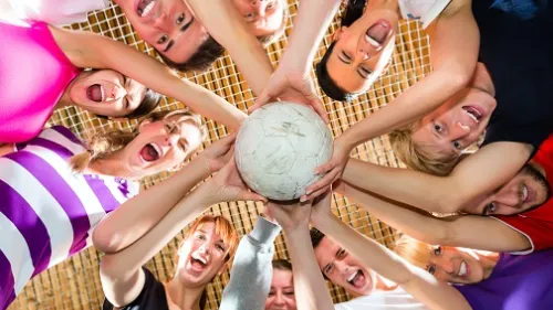 Viele Hände halten einen Ball und elf Menschen schauen nach unten