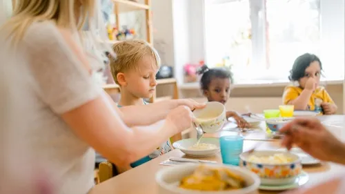 Drei Kinder und eine Erzieherin sitzen am Frühstückstisch