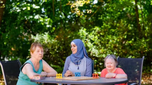 Zwei Seniorinnen und eine Mitarbeiterin spielen Mensch ärgere dich nicht im Freien