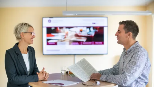 Zwei Menschen vor einem Bilschirm mit Unterlagen